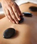 Hands massaging lower back with warm stones. You may also like: